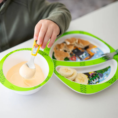 Child using a spoon with a bowl and plate featuring cartoon characters on a white surface.