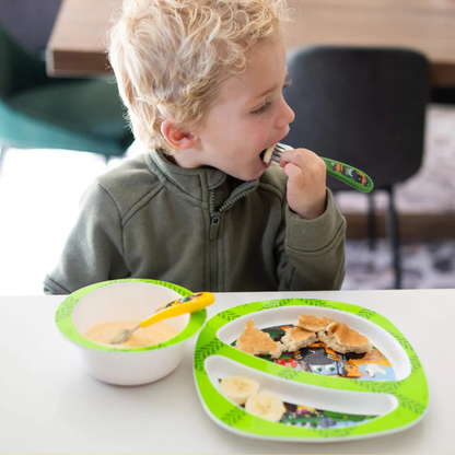 Child eating with a fork and knife at a table, using a green plate and bowl set.